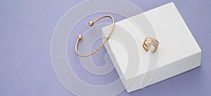Panoramic shot of gold bracelet and ring on white box on purple background