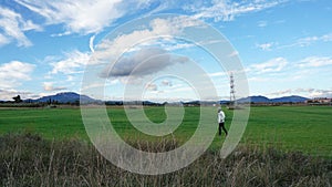 Panoramic shot of a man walking in the green field under a blue cloudy sky