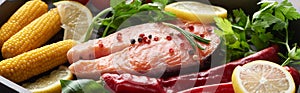 Panoramic shot of raw salmon steak with lemon, herbs and vegetables.