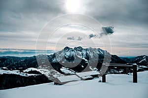 Panoramic shot of a snow covered cabin with a beautiful view of snow capped mountains