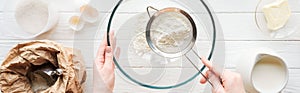 Panoramic shot of woman sieving flour in bowl on table with ingredients.