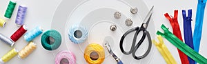 Panoramic shot of zippers, scissors, thimbles, threads, knitting yarn balls, bobbins, tracing wheel on white background.