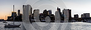 Panoramic skyline of Boston cityscape with its skyscrapers and sailboats at its harbor at sunset