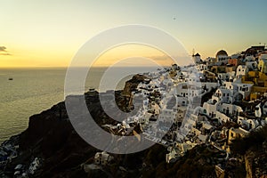 Panoramic skyline scene in sunset light of Oia windmill and white building townscape along island natural mountain facing ocean