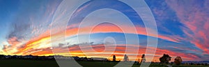 Panoramic striking sunset background with vivid orange, blue, red and yellow, in the shape of a rainbow.