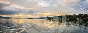 Panoramic summer view of boat cruise excursion landscape on Zurichsee with beautiful sunset shining light through clouds reflected