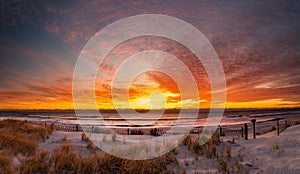 Panoramic sunrise at the beach with a dune fence in the foreground