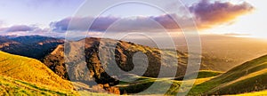 Panoramic sunset view of hills and valleys in the Diablo mountain range starting to turn green; San Jose and bright light from the