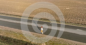 panoramic top view of woman running along an asphalt road among the fields in sunny day