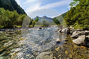 Panoramic valley landscape with crystal clear river, stones, and tall trees in Ordesa Pirineos. Reflections in the water and
