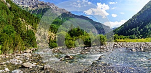 Panoramic valley landscape with crystal clear river, stones, and tall trees in Ordesa Pirineos. Rest and camping area to enjoy photo