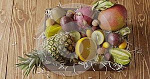 Panoramic video top view on a box with variety fresh natural organic exotic fruits on a wooden background. Slow motion