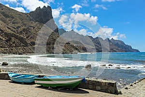 Panoramic view of Aimasiga beach with volcanic black sand and lone rocks sticking out of the sea foam. Local fishing boats in the