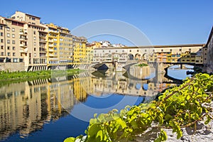 Panoramic view of the Arno River and stone medieval bridge Ponte Vecchio with beautiful reflection of colorful houses, Florence