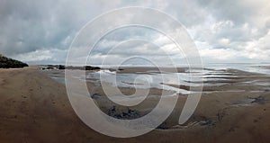 Panoramic view of the beach at sandsend near whitby at low tide with a dramatic stormy cloudy sky reflected in pools of water