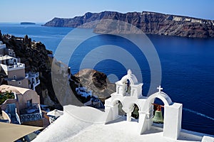 Panoramic view of beautiful blue Aegean sea and caldera from Oia village with white church foreground, buildings along island