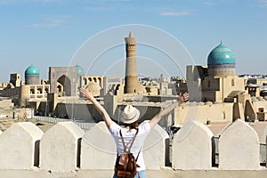 Panoramic view of Bukhara, young woman tourist with arms raised in front of Bukhara city - Uzbekistan