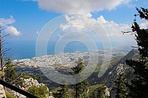 Panoramic view from the castle of Saint Hilarion through the branches of trees to the city of Kyrenia, the mountains, the sky and