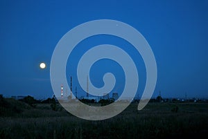 A panoramic view of the chimneys and cooling towers of the CHP plant against the background of the night sky and the full moon