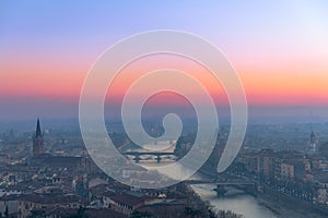 Panoramic view of the city of Verona and the Adige river with bridges covered with the evening mist colored by the setting sun.