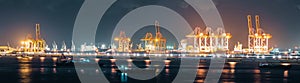 Panoramic view of cranes loading shipment containers in cargo shipping port at night, banner size. Logistic industry concept
