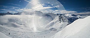 Panoramic view down snow covered valley in alpine mountain range with sundog