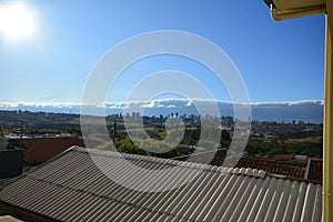 Panoramic view of downtown with sun, cold front clouds and house roofs in the foreground, blue sky, wide angle