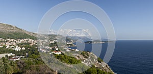 Panoramic view of Dubrovnikâ€™s coastline, with its clear blue waters and lush green cliffs, under a sky with clouds
