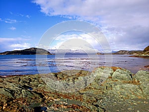 Panoramic view of extreme landscape of Argentine Patagonia. Snowy mountain ranges, frozen lake and rocks foreground under cloudy