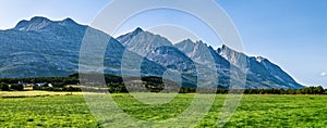 Panoramic view at five of Seven Sisters Mountain range on Sandnessjoen, ideally green grass, small Norwegian village and mountains