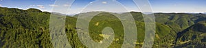 Panoramic view of forested hills and a glade on a bright day.