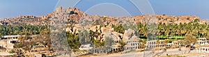 Panoramic view of the Hampi ancient ruins, mountain formations and gardens with palm trees