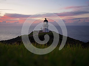 Panoramic view of historic white Cape Reinga lighthouse landmark on oceanside clifftop during sunset in New Zealand