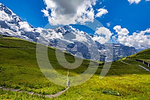 Panoramic view of idyllic mountain scenery in the Alps with fresh green meadows in bloom on a beautiful sunny day in summer,