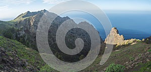 Panoramic view of illuminated sharp rock and cliffs on top of La Merica mountain with cacti, pine and palm trees. Camino