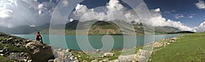 panoramic view of lake and mountain.mountain landscape with touching clouds. Boy sitting on boulder.