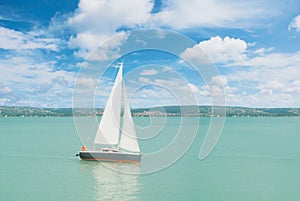 Panoramic view of lake river blue transparent water, a white sport modern luxury yacht sail boat floating and a green shore with