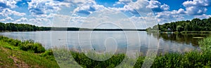 Panoramic view of the lake on a sunny day. Floating sailboats and a forest in the background. Paprocany Lake, Tychy, Poland