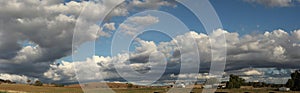 Panoramic view of large open dry drought affected farm fields under stretching cloud filled blue skies with farm buildings in