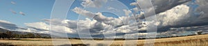 Panoramic view of large open dry drought affected farm fields under stretching cloud filled blue skies over properties in rural