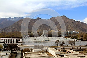 The panoramic view of Lhasa city, in front of Potala Palace and Palace square, with modern building and mountains, far away a Tib
