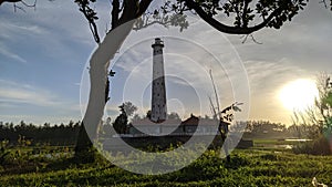 panoramic view of the lighthouse and the sky at dusk from behind the trees sun green sky blue orang