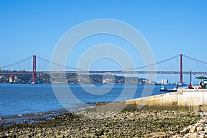 Panoramic view of Lisbon\'s red metal 25 de April steel suspension bridge like the Golden Gate, from the beach coast.