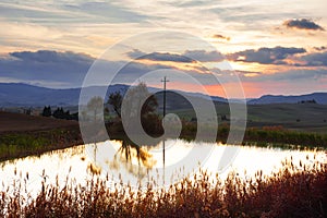 Panoramic view of a little pond, rolling hills, sky and clouds at sunset in tuscan countryside landscape, Tuscany, Italy