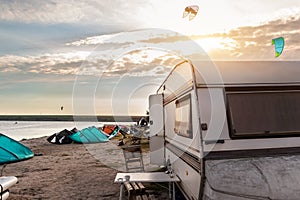 Panoramic view of many surf board kite riders on sand beach watersport spot bright sunny day against old rv camper van