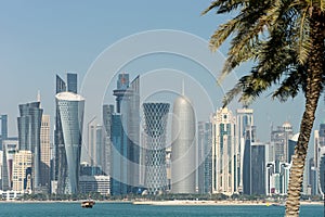 Panoramic view of modern skyline of Doha through blurred palm trees. Qatar on sunny day