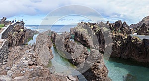 Panoramic view of the natural pools on village of Porto Moniz, formed by volcanic rocks, islet of Mole in the background