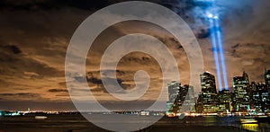 Panoramic view of New York skyscrapers illuminated at night against the sea under a cloudy sky