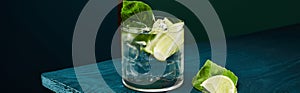 Panoramic view of old fashioned glass with fresh drink, mint leaf and lime slice on blue wooden surface