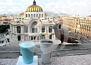Panoramic view of the palace of fine arts in mexico city with bird, coffee and blue drink in the foreground